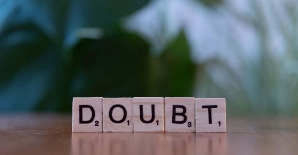 Close-up of Scrabble tiles spelling 'doubt' on a wooden surface, conveying uncertainty.