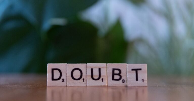 Close-up of Scrabble tiles spelling 'doubt' on a wooden surface, conveying uncertainty.